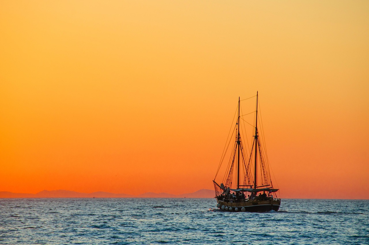 An image of an old sailing ship at sea with a golden sky behind